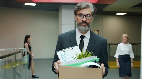 Sad Office Worker Walking in Hallway with Carton Box Leaving Work After Employment Termination alt