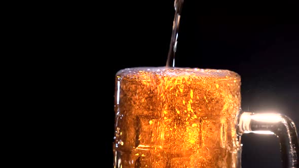 Low Angle of Soft White Foam Rising and Spilling From Glass Cup of Cold Beer on Black Background alt