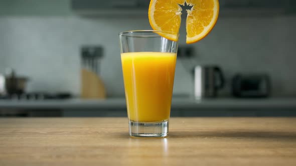 Female hand puts orange slice and straw into glass with orange juice. Healthy drink on wooden table