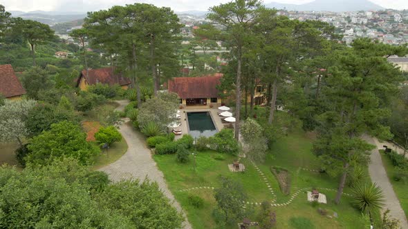 Aerial drone flying around the swimming pool between the pine trees with nice city landscape at back alt