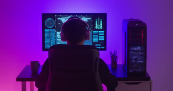 Man Programmer in Headphones Working at a Computer in Data Center at Night alt