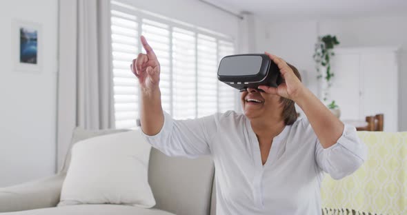Happy african american senior woman sitting on couch enjoying using vr headset alt