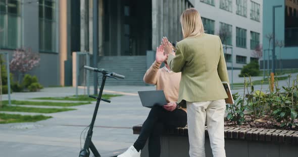 Man and Woman Sitting on Bench by Modern Office Building in Smart Casual Business Style alt