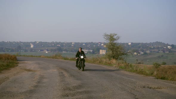 Front View of a Stylish Cool Young Man in Sunglasses and Leather Jacket Driving His Chopper on a alt
