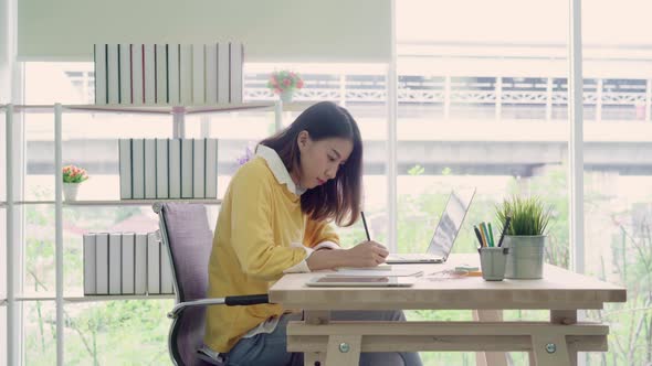 young smiling asian woman working laptop on desk in living room at home. alt