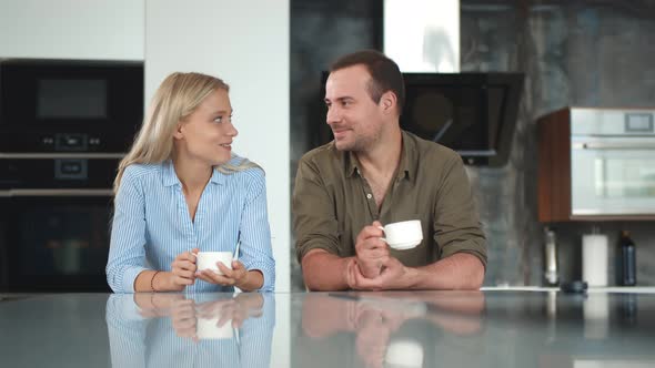 Cute Young Couple Drinking Coffee in Kitchen and Chatting During Breakfast alt