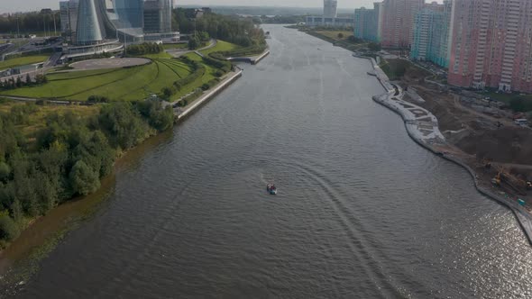 Motor Boat Goes Along the River in a Picturesque Cityscape in Summer alt
