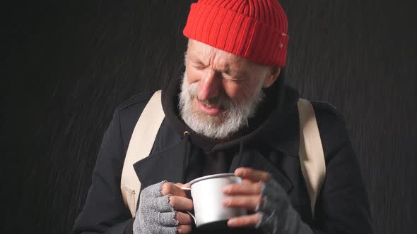 Homeless Mature Bearded Man Stands in the Rain Holding a Cup To Collect Money alt