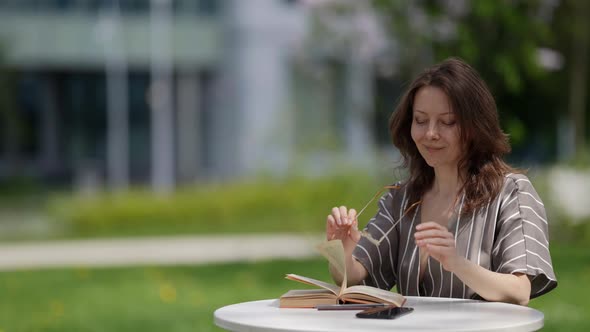 a Brunette in a Striped Dress is Sitting at a Table on the Street alt