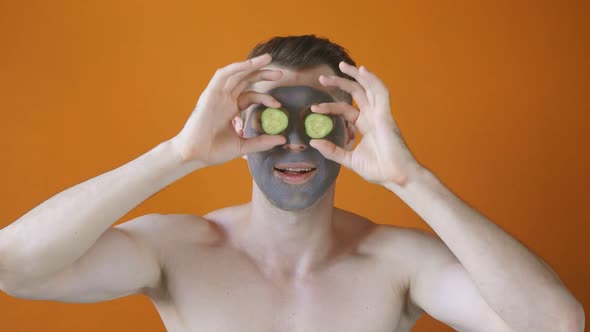 Young Man Uses a Gray Clay Face Mask with Cucumber Slices Expresses Positive Emotions Isolated