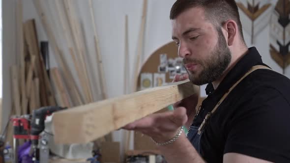 Strong Male Carpenter with a Beard in a Carpentry Workshop While Working alt