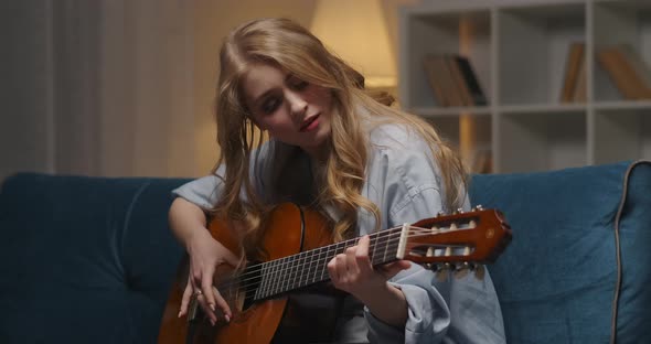 Pretty Young Female Musician Is Composing Music and Playing Guitar at Home at Evening Medium alt