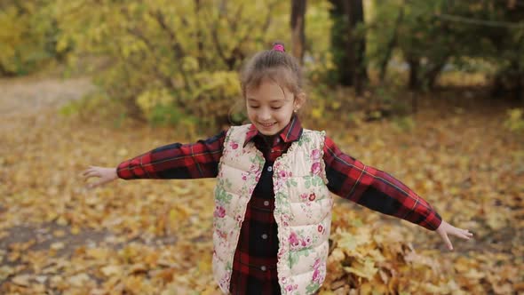 A Little Girl Plays with Yellow Leaves and Falls Into Them