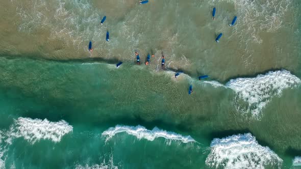 Aing drone video looking down at a large group of surfers catching waves at the beach alt