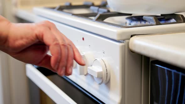 Hands of Senior Caucasian Woman Turning Off White Domestic Gas Stove with White Enameled Kettle