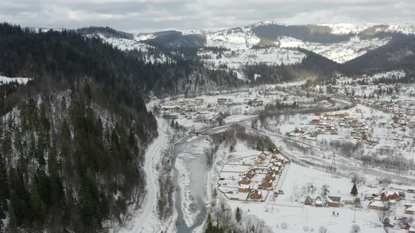 Aerial view of a Mountain Village with Hills Covered in Snow