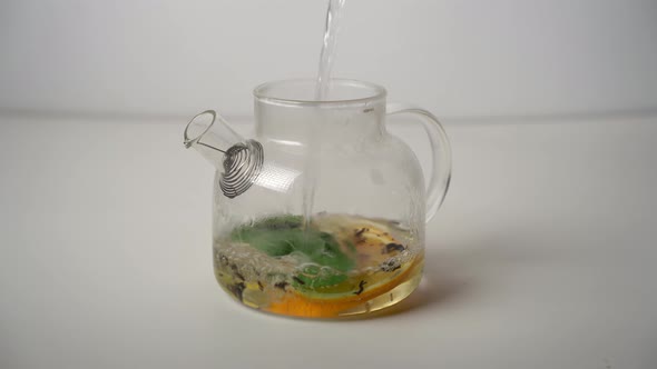 Pouring boiling water into the teapot with lemon, mint leaves and black tea.