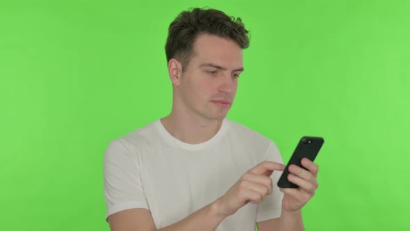Young Man Browsing Smartphone on Green Background alt