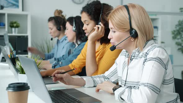 Group of Women Call Center Workers Talking Using Headphones and Laptops Working Indoors in Office alt