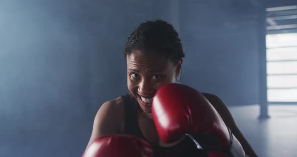 African american woman wearing boxing gloves training throwing punches in empty room alt