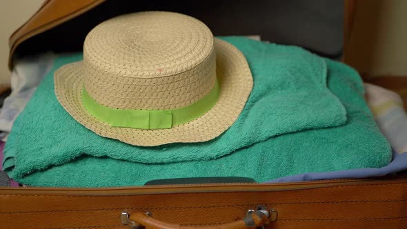 Hand unpacking straw hat from suitcase close up shot alt