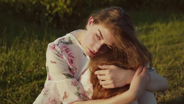 Thoughtful Girl Sitting in Pose with Leaned Head on Knees Among Green Field alt