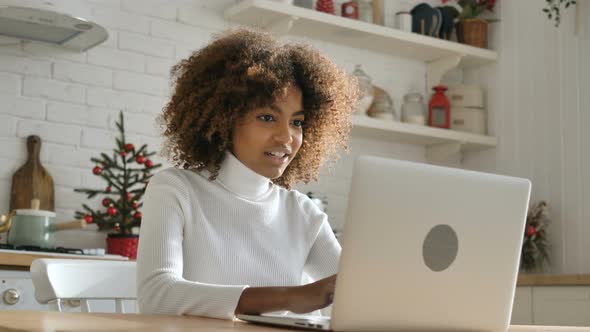 Dark Skinned Freelancer Looks at Notebook Screen and Smiles alt