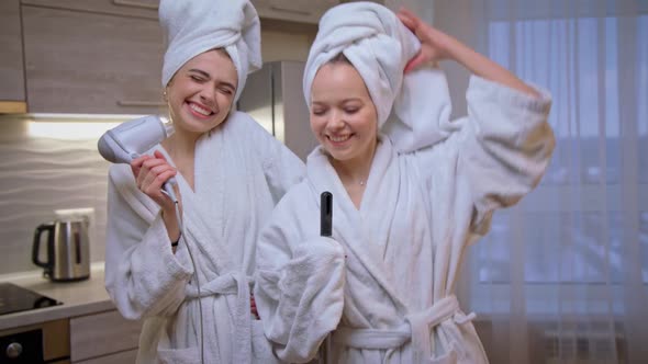 Two Girl Friends in White Bathrobe Dance Sing and Dry Hair with Hairdryer Laugh