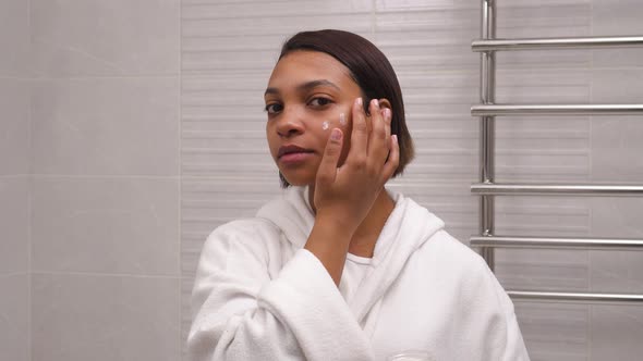 A Young Beautiful Woman with Dark Skin Uses a Facial Moisturizer