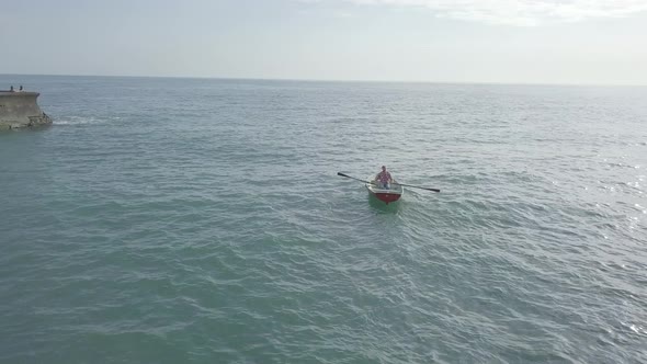 Aerial view of fisherman rowing oars in small fishing boat floating in open sea. Sunlight on water