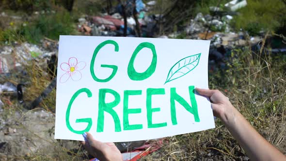 Go Green Phrase on Cardboard in Person Hands Against Open Dumping Background alt