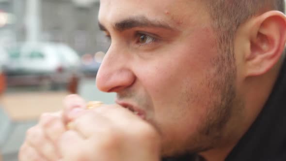Close up of young man eating tasty burger in street food cafe alt