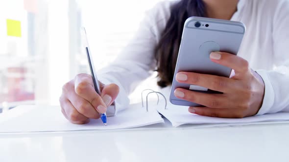 woman using smartphone and taking notes alt