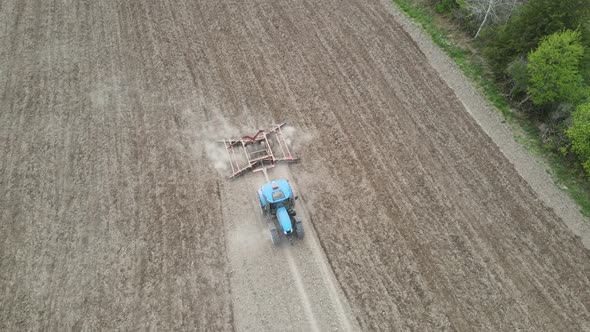 Birds eye view of farmer tilling field in preparation for planting. Discing of dry soil with dust.