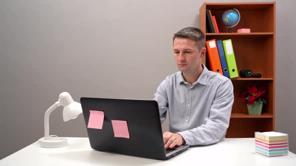 Professional Man Typing on a Laptop Computer and Grabbing a Sticky Note That is on His Desk of His