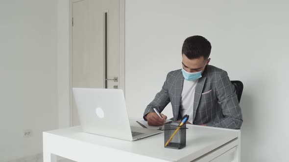 Male Student in Medical Mask Working with Laptop at Table During Remote Studying alt