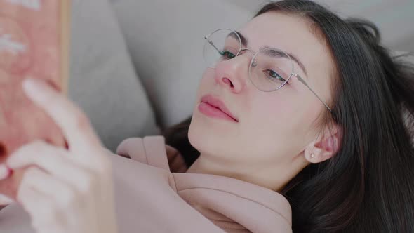 Close up of young caucasian woman wearing reading glasses reading a book.