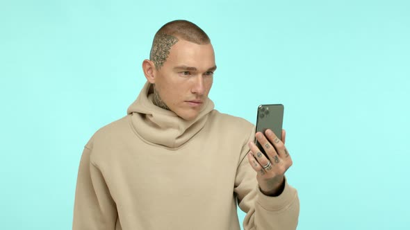 Cool Tattooed Guy with Shaven Head and Pierced Nose Wearing Hoodie Looking at Smartphone Surprised