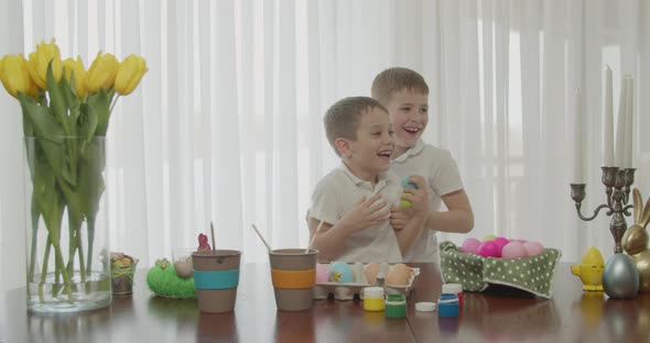 Two Little Brothers are Smiling Tickling Each Other While Painting Easter Eggs alt
