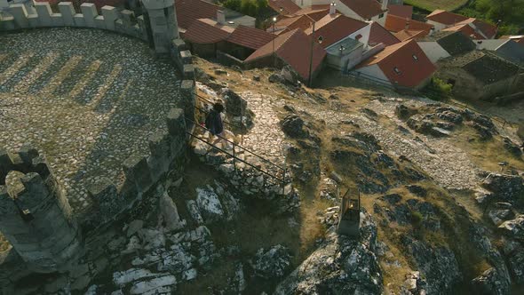 A girl walks down the stairs of the stone path at Folgosinho Castle as a group of tourists walk up a alt