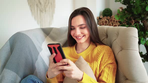 Woman Smiling Hold Smartphone Watching Social Media Stories Video Sit on Sofa alt