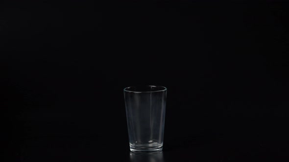 Pour Clean Water From a Plastic Bottle Into a Misted Glass Glass Beaker on a Black Background