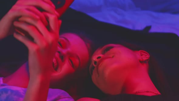 Two young girls lying on the floor while taking selfies alt