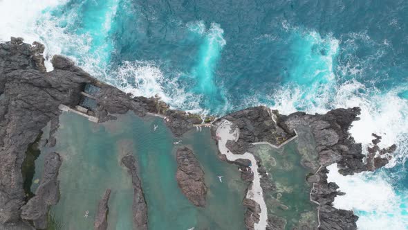 Overhead View Of People Swimming On Natural Swimming On Lava Rock In Porto Moniz, Madeira, Portugal. alt