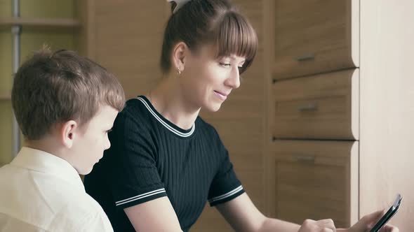CU: Young Pretty Mother Shows Her Son How To Do Homework, Uses a Tablet Computer. alt