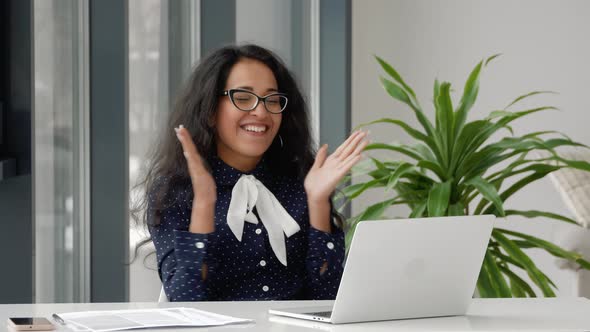 Beautiful mixed race Businesswoman Sitting at Her Office Desk, Raising Her Arms and Applauds in Cele