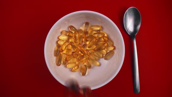 Oval Yellow Pills Fall Into Plate Standing on Red Table with Metal Spoon