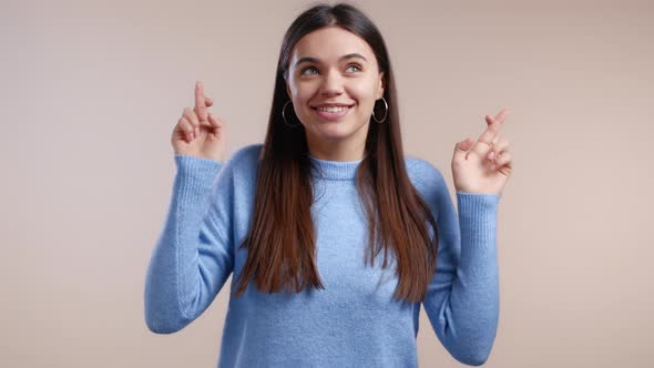 Cute Young Woman in Blue Sweater Praying with Crossed Fingers Over White Background alt