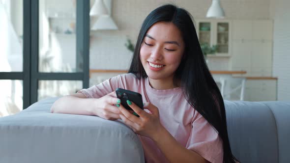 Front View of a Serene Happy Darkhaired Asian Woman Using Her Smartphone for Texting Browsing Mobile alt