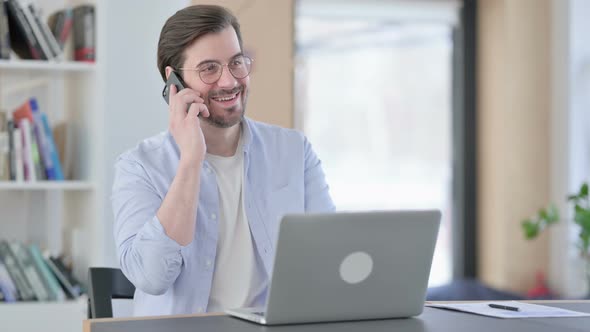 Man in Glasses with Laptop Talking on Smartphone alt